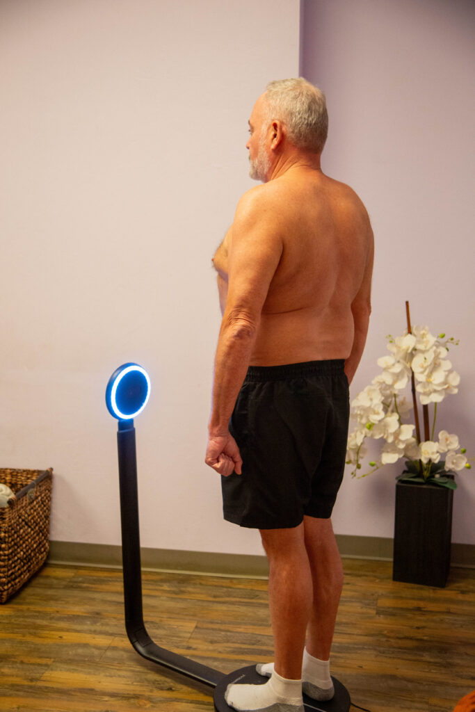 A shirtless man stand gets an InBody Scan procedure at Petra's Weightloss Clinic.